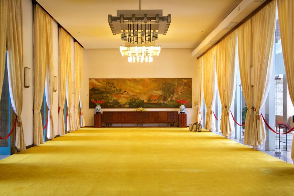 A hallway with a yellow carpet, a chandelier, and a painting on the wall.