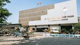 Un edificio de museo con un cartel en idioma extranjero, rodeado de plantas en macetas y una exhibición de aviones militares.