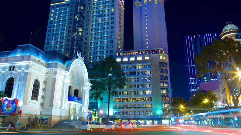 A brightly lit urban scene with a historic building, modern high-rises, and a busy street at night.