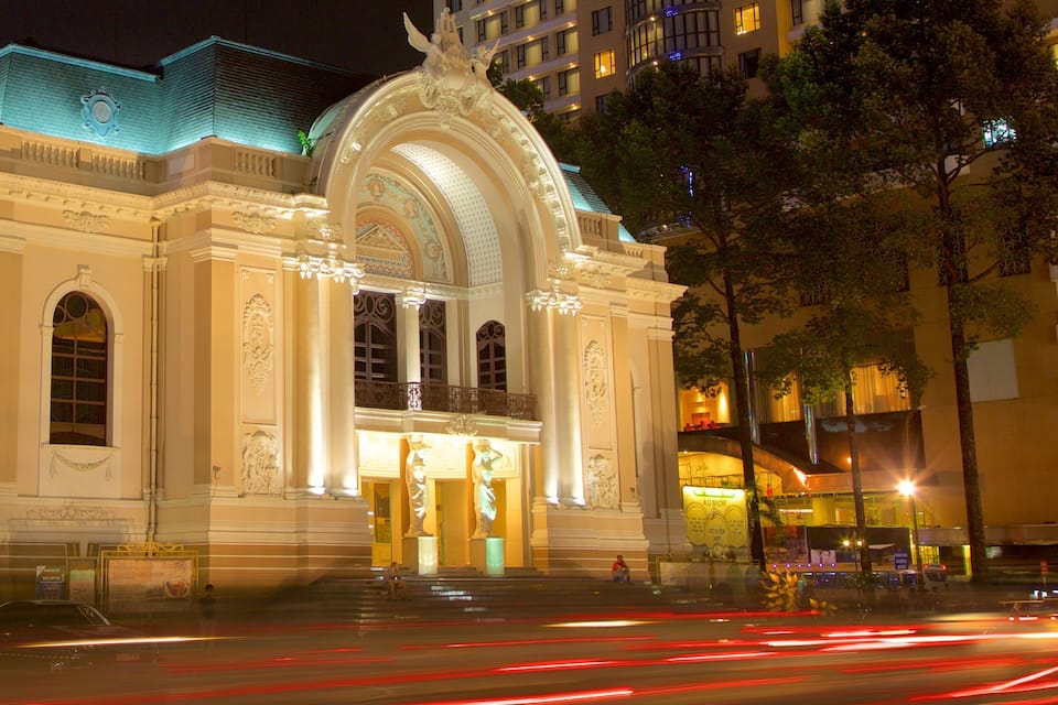 A grand building with ornate architecture and a blue roof, surrounded by trees and modern buildings.
