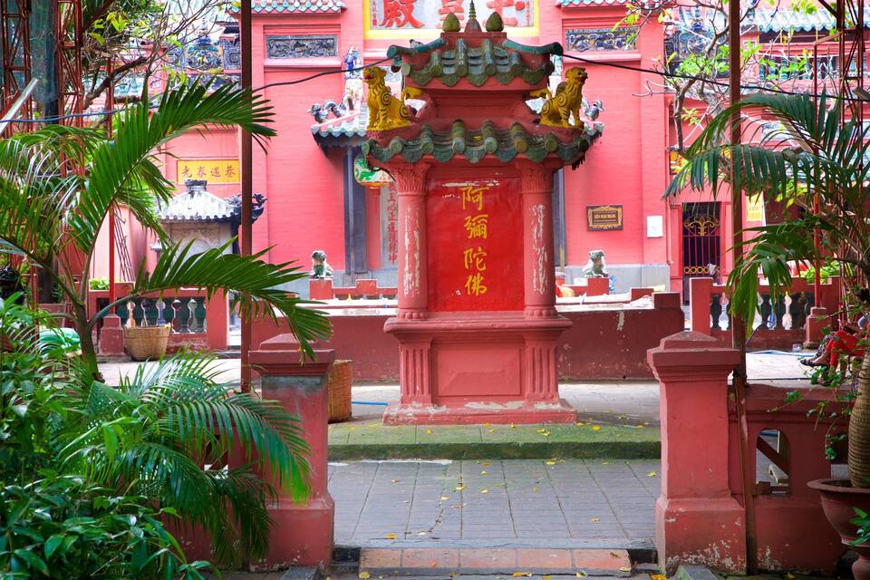 A traditional Chinese gate with a lion statue, surrounded by lush greenery and red walls.