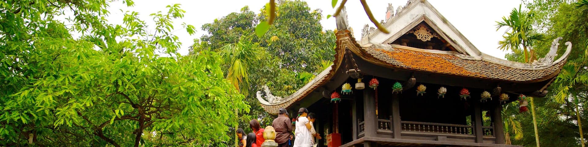 A traditional pavilion with a tiled roof, surrounded by lush greenery and a calm water body.