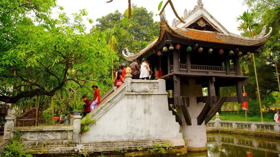 A traditional pavilion with a tiled roof, surrounded by lush greenery and a calm water body.