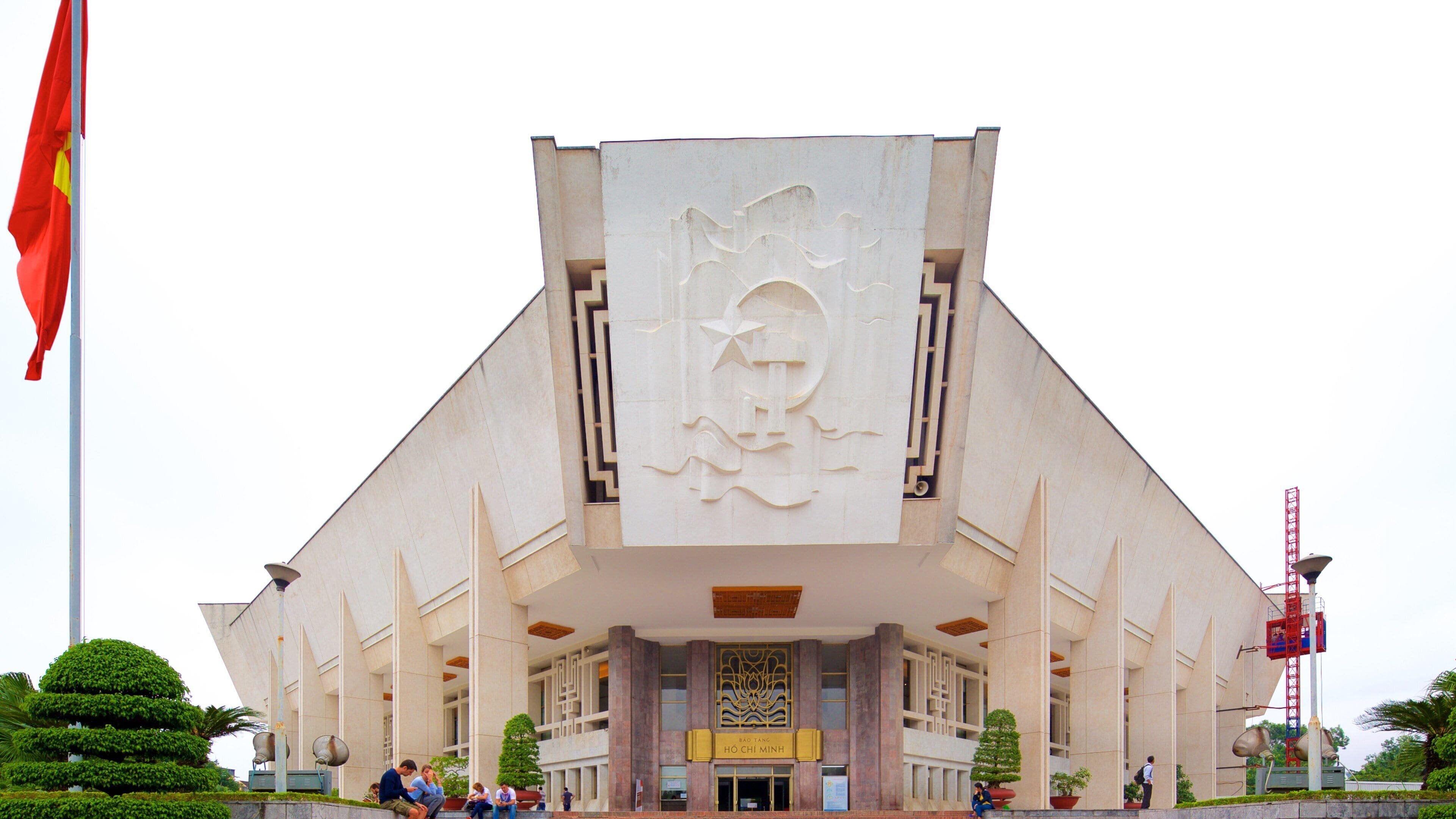 A large, modern building with a prominent entrance and a large flag on a flagpole to the left.
