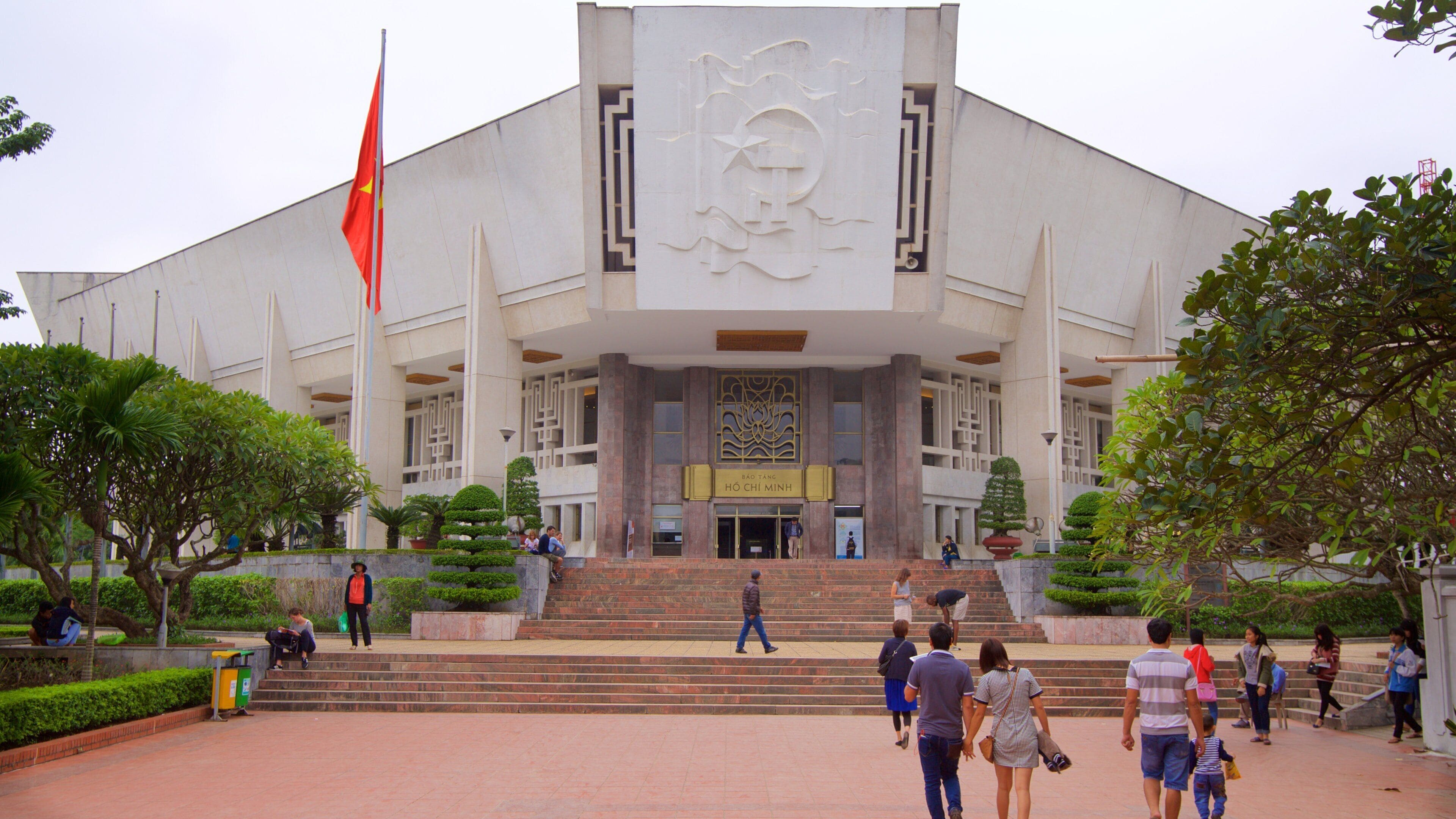 A large building with a prominent entrance, steps leading up to it, and a flagpole with a flag.