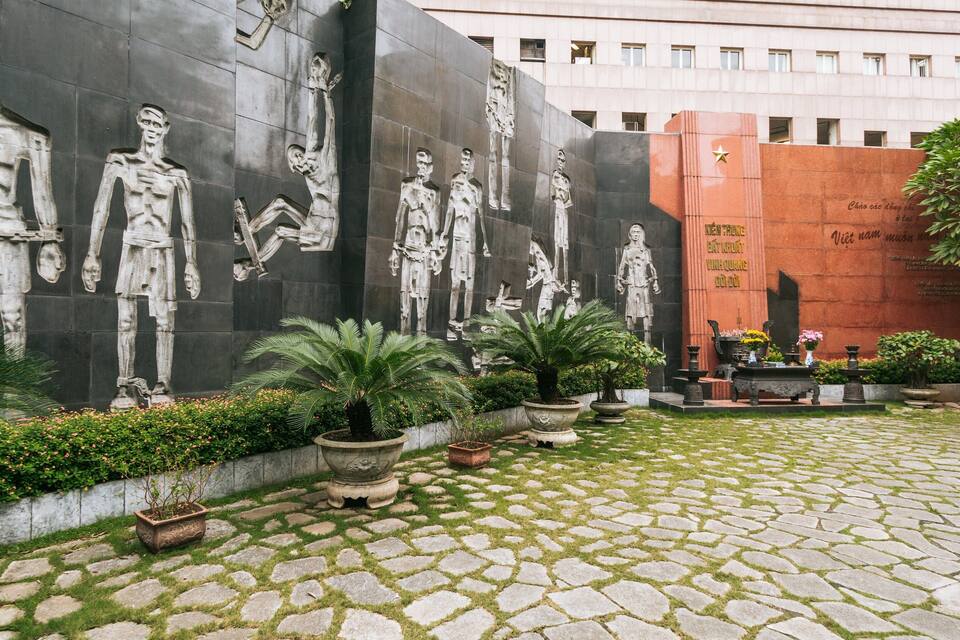 A courtyard with stone tiles, potted plants, and a large mural of human figures.