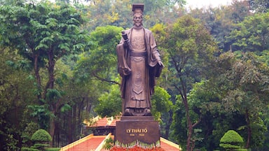 Una estatua de una figura histórica en un jardín exuberante con un pabellón de techo rojo.