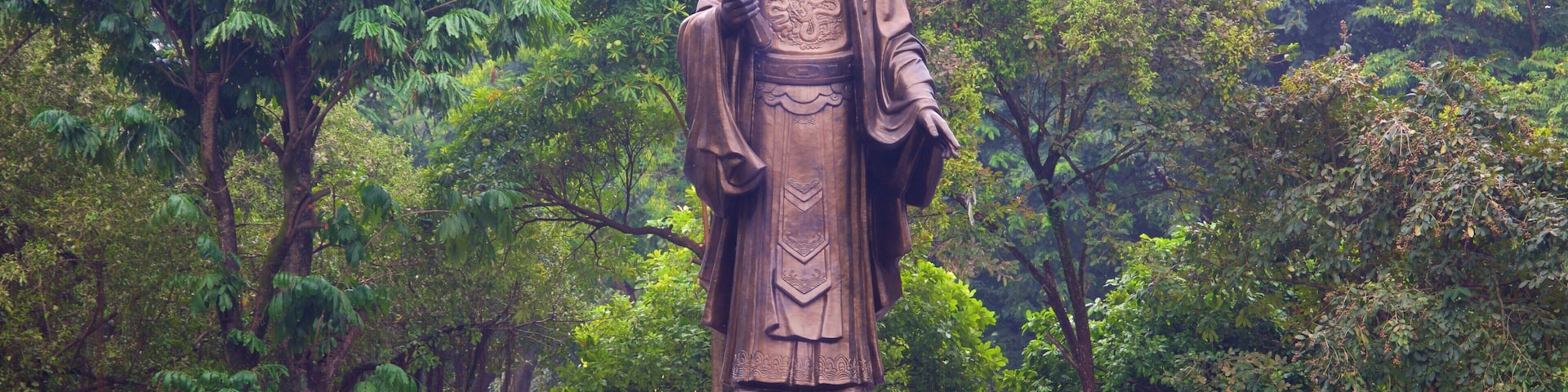 A statue of a historical figure in a lush garden with a red-roofed pavilion.