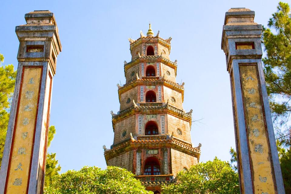 Un pagode a più livelli con complesse decorazioni in mattoni e ornamenti elaborati, circondato da vegetazione lussureggiante.