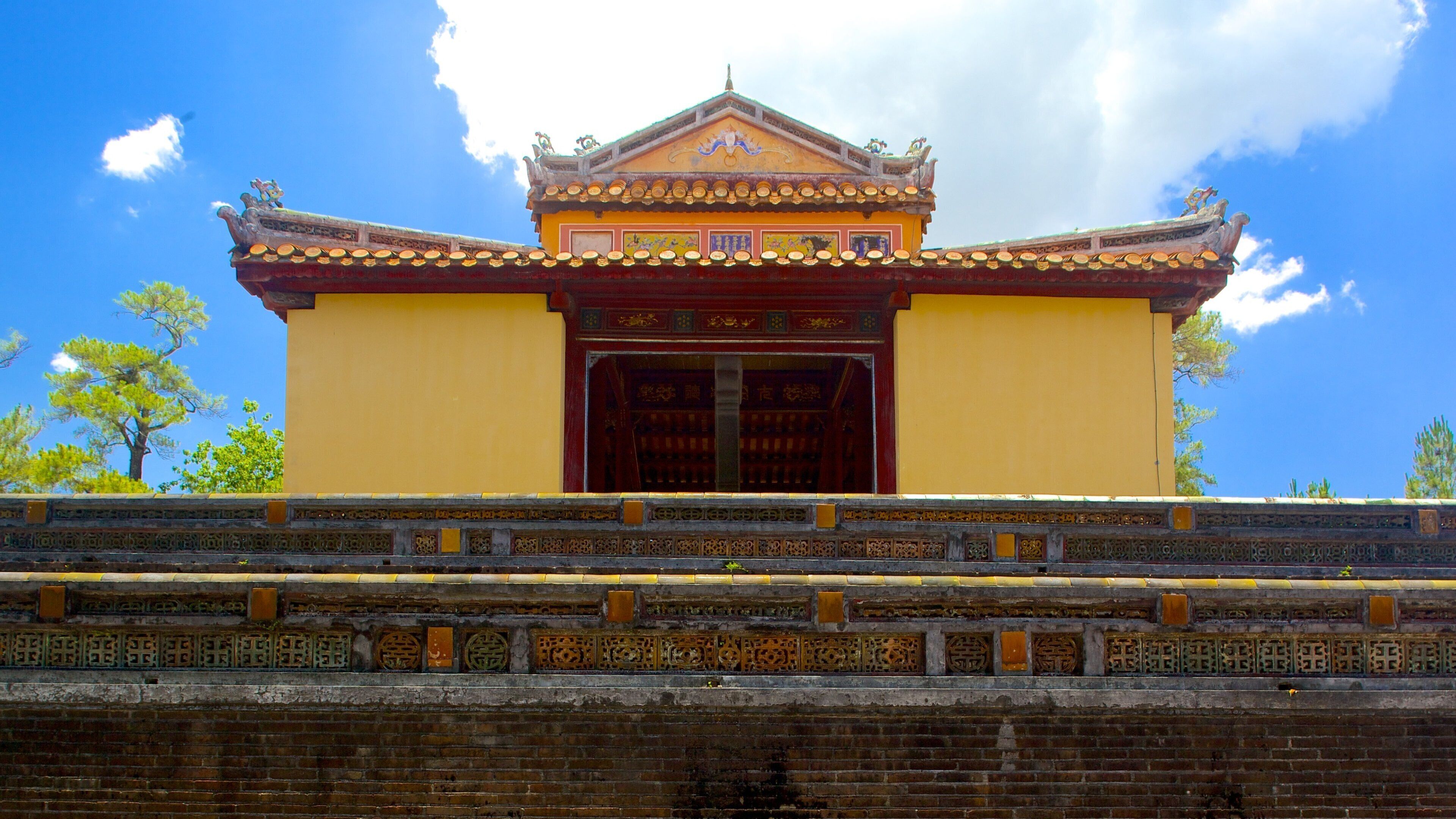 Un bâtiment traditionnel chinois, caractérisé par une façade jaune, un toit richement décoré et une grande porte rouge.