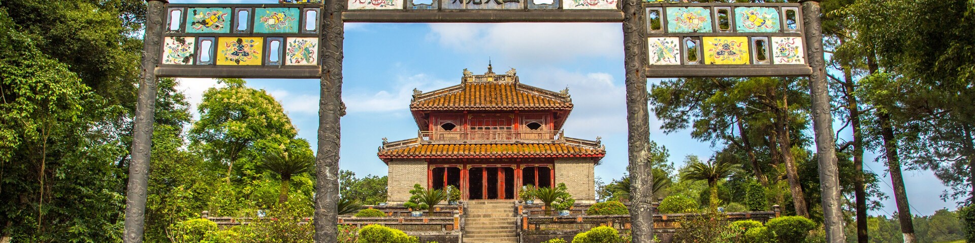 Une porte chinoise traditionnelle, ornée de carreaux colorés, avec un temple en arrière-plan.