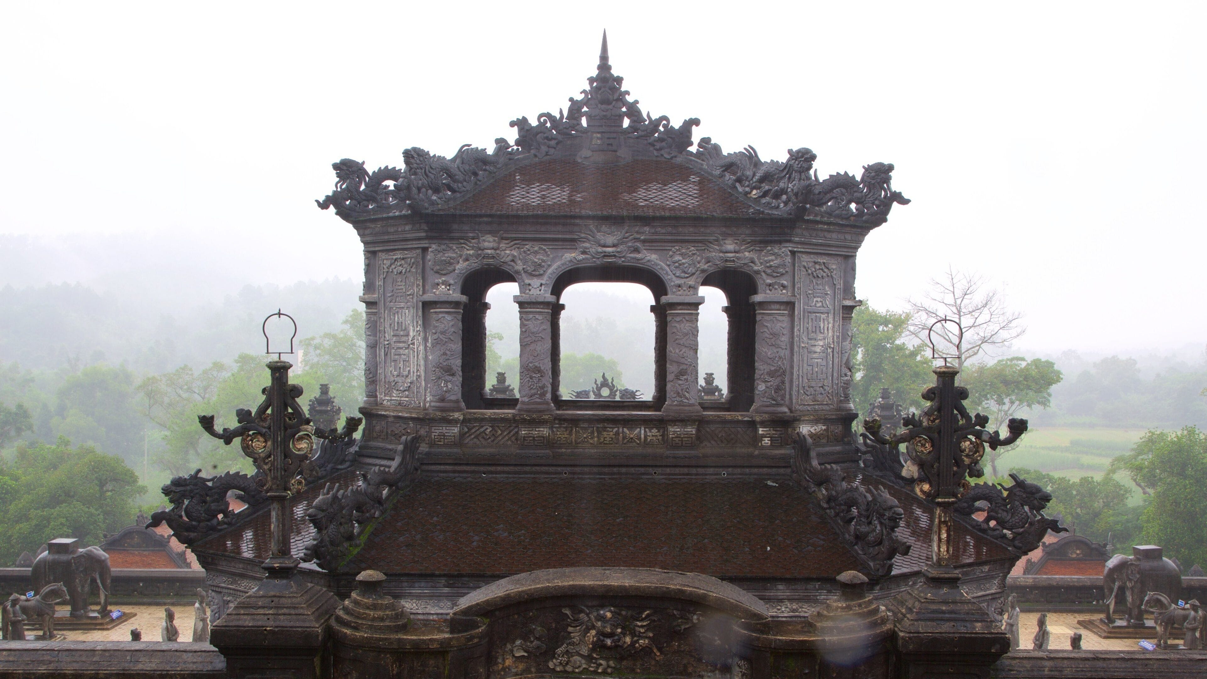 A historic stone structure with intricate carvings and lion statues, set against a misty landscape.