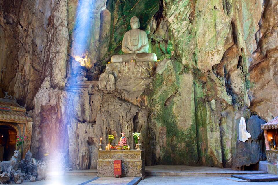 A cave temple with a seated Buddha statue, a small shrine, and a waterfall.