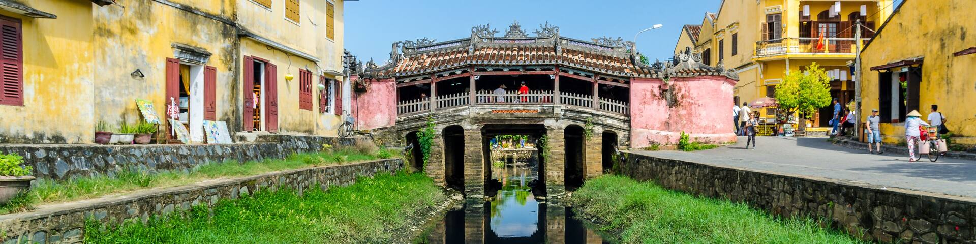 A traditional bridge with ornate railings, a canal reflecting the buildings, and a clear blue sky.