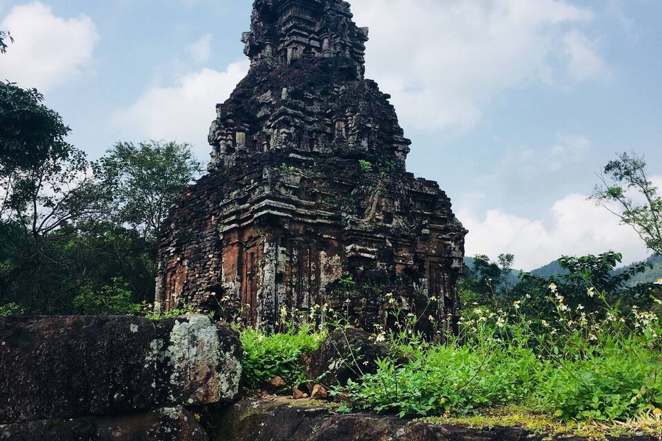 An ancient temple with intricate carvings, surrounded by lush greenery and a stone wall.