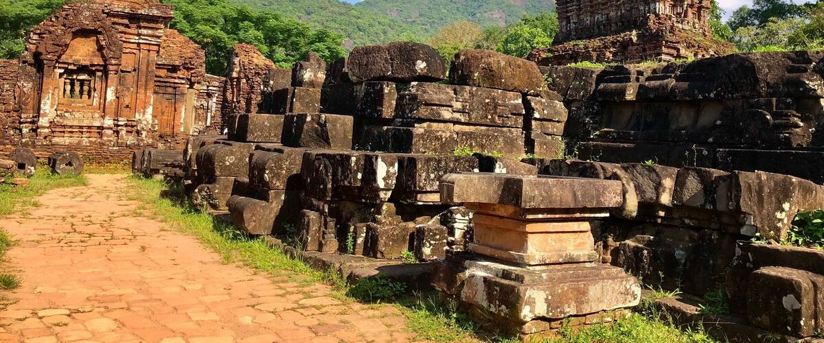 Ancient stone ruins with a pathway leading through them, set against a backdrop of lush green hills.