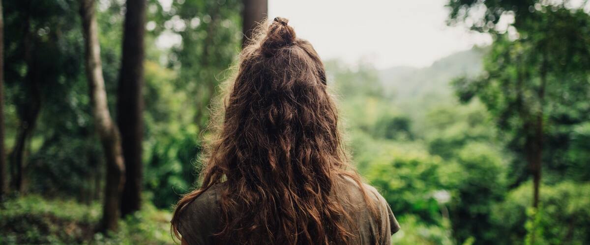 A person with long hair standing in a forest.