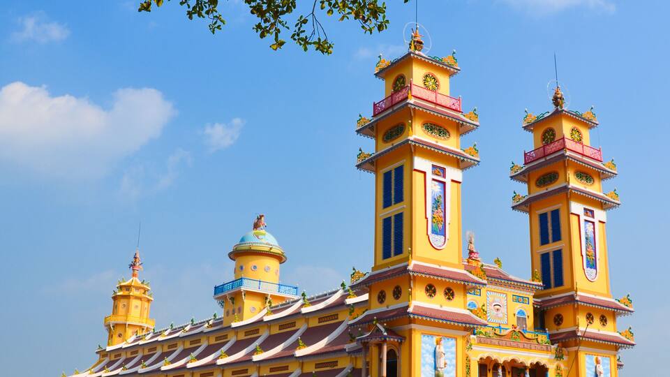 A vibrant yellow temple with multiple towers and intricate designs, surrounded by a clear blue sky.