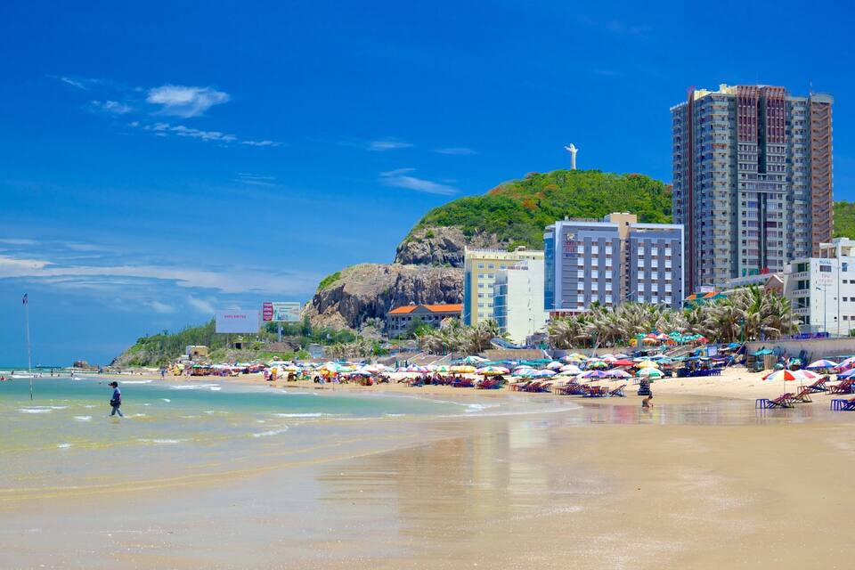 A beach with umbrellas, a statue, and buildings.