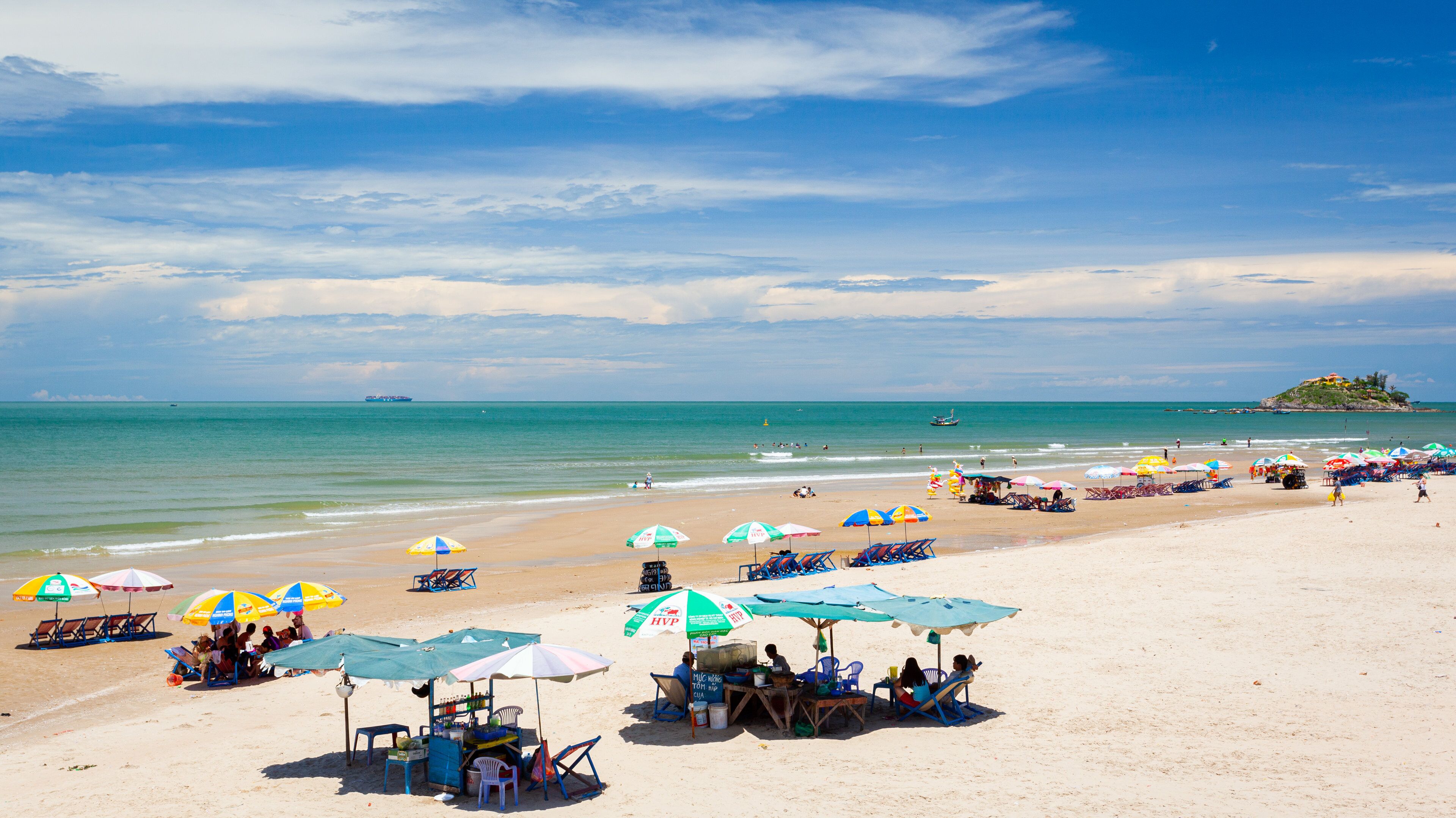 Een strand met parasols, stoelen en een eiland in de verte.