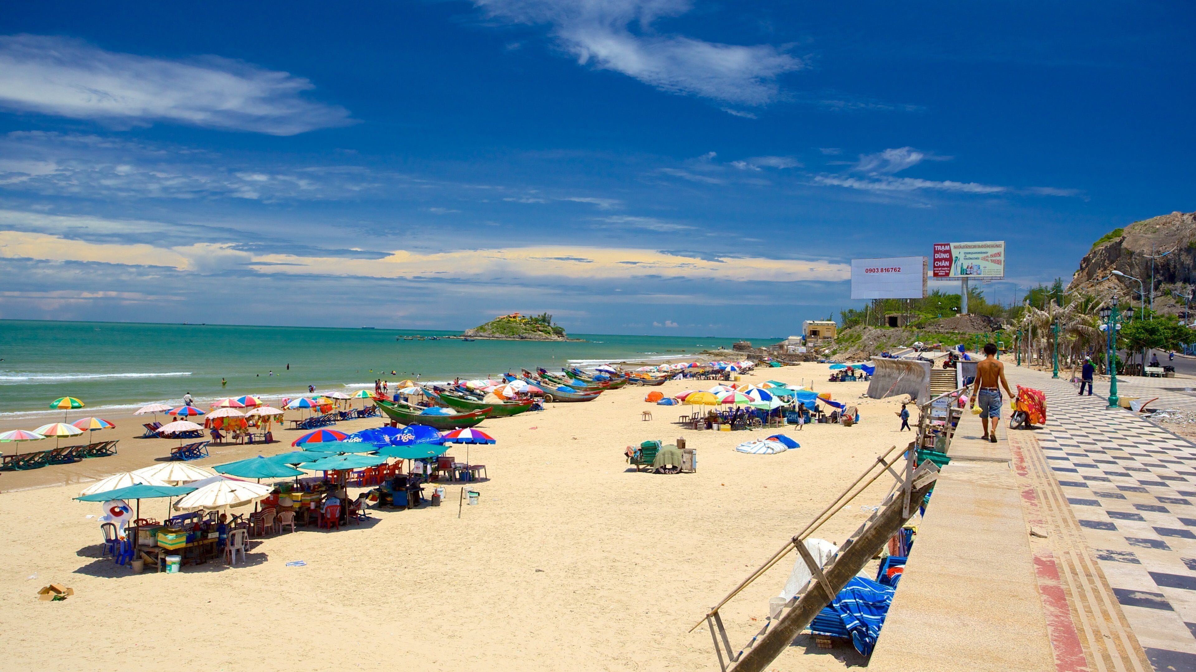 A beach with colorful umbrellas, boats, and a distant island.