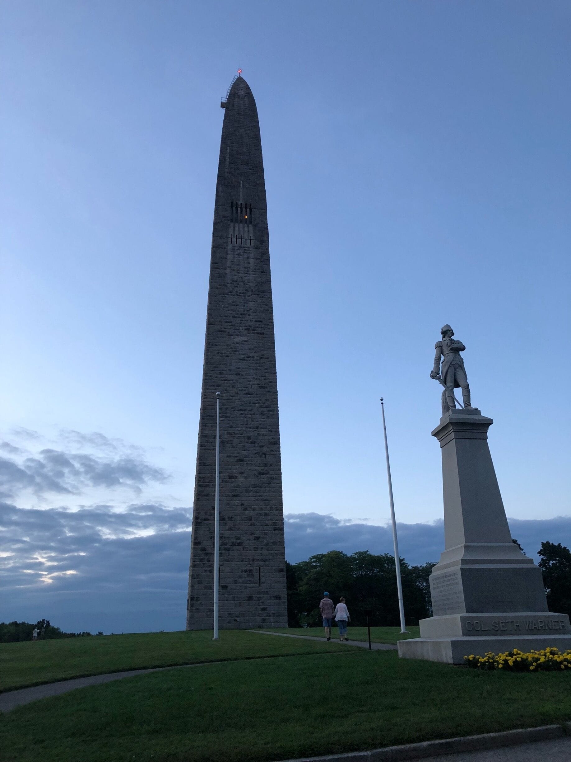A tall obelisk and a statue in a park.