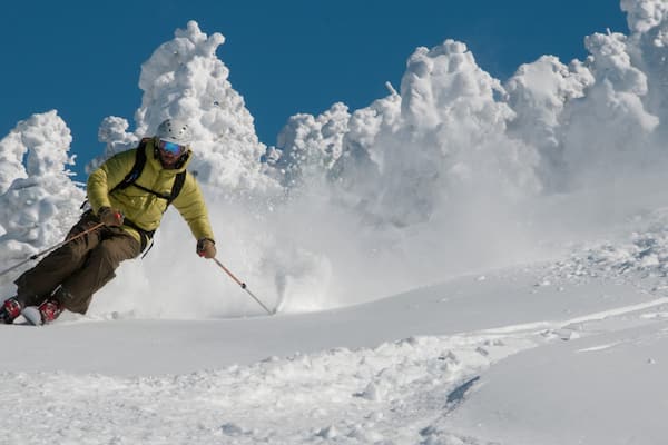 Un skieur, vêtu d’une veste jaune et d’un casque, descend une pente enneigée.