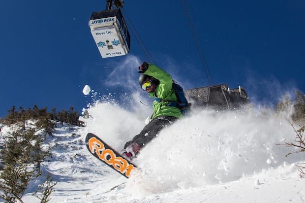 A snowboarder performing a jump with a cable car in the background.