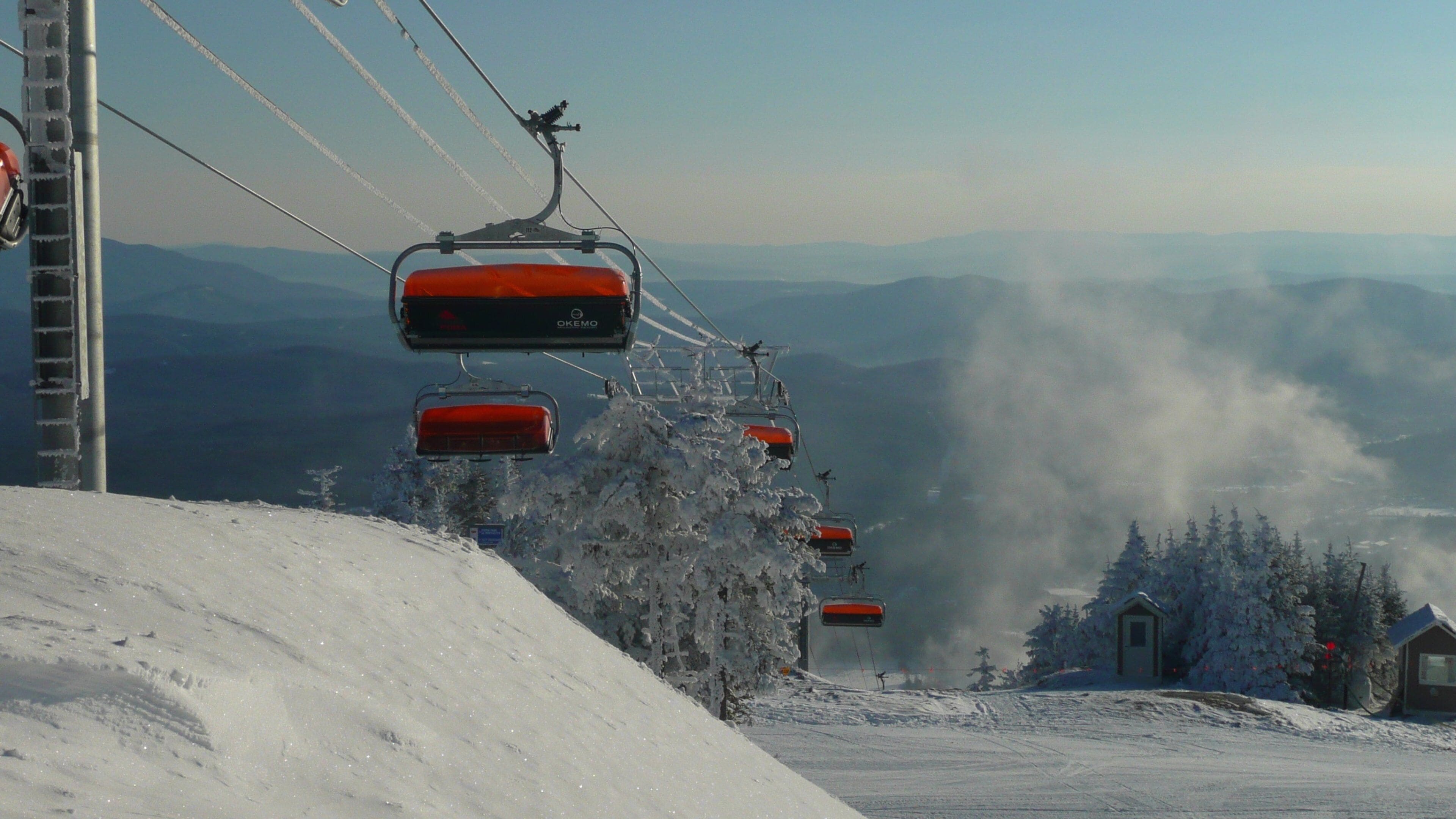 A ski lift with red chairs, snow-covered trees, and a mountain landscape in the background.