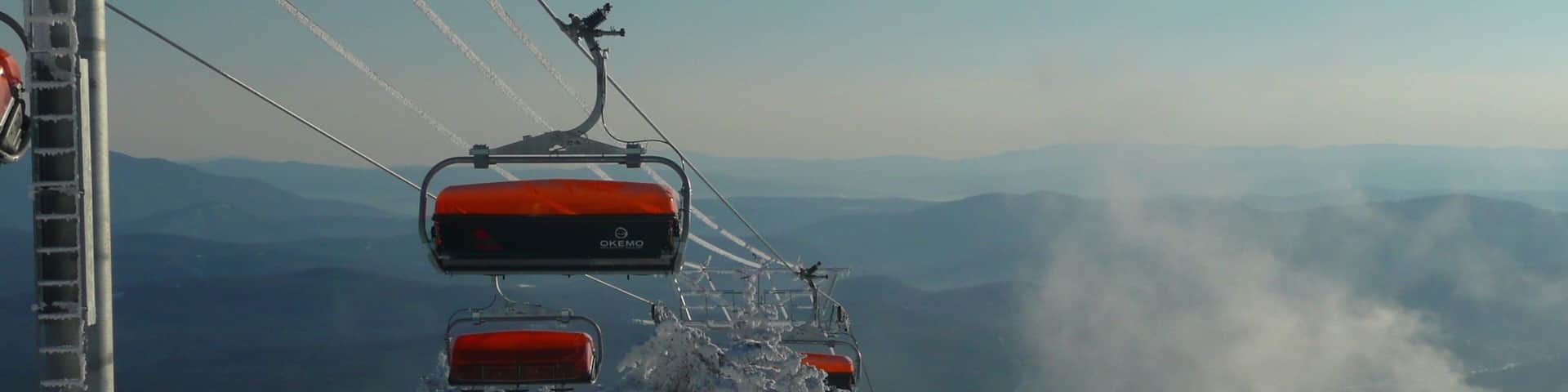 A ski lift with red chairs, snow-covered trees, and a mountain landscape in the background.