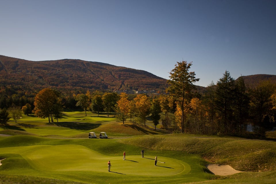 Camp de golf amb turons ondulats, arbres de tons tardans i una muntanya al fons.