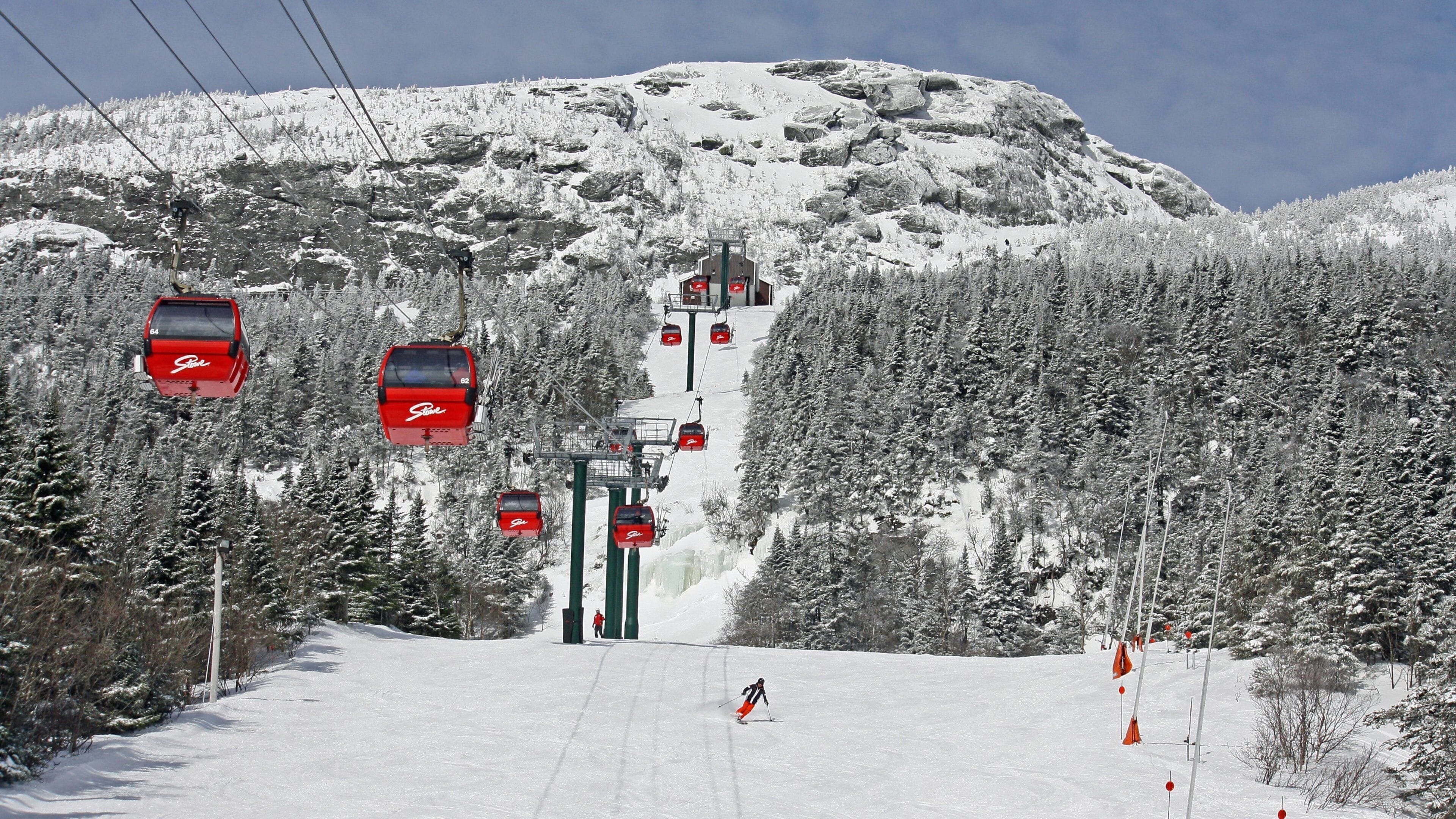 A ski lift with red gondolas ascending a snowy mountain slope.