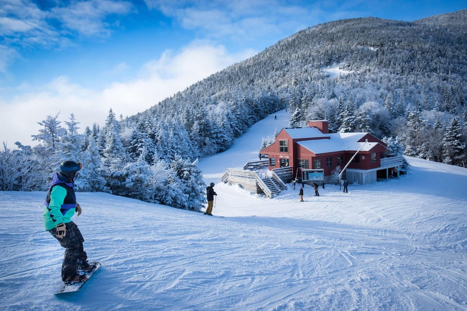A snow-covered ski slope with a red lodge and a person snowboarding.