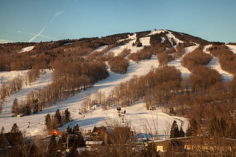 A snow-covered ski slope with a ski lift, trees, and buildings.
