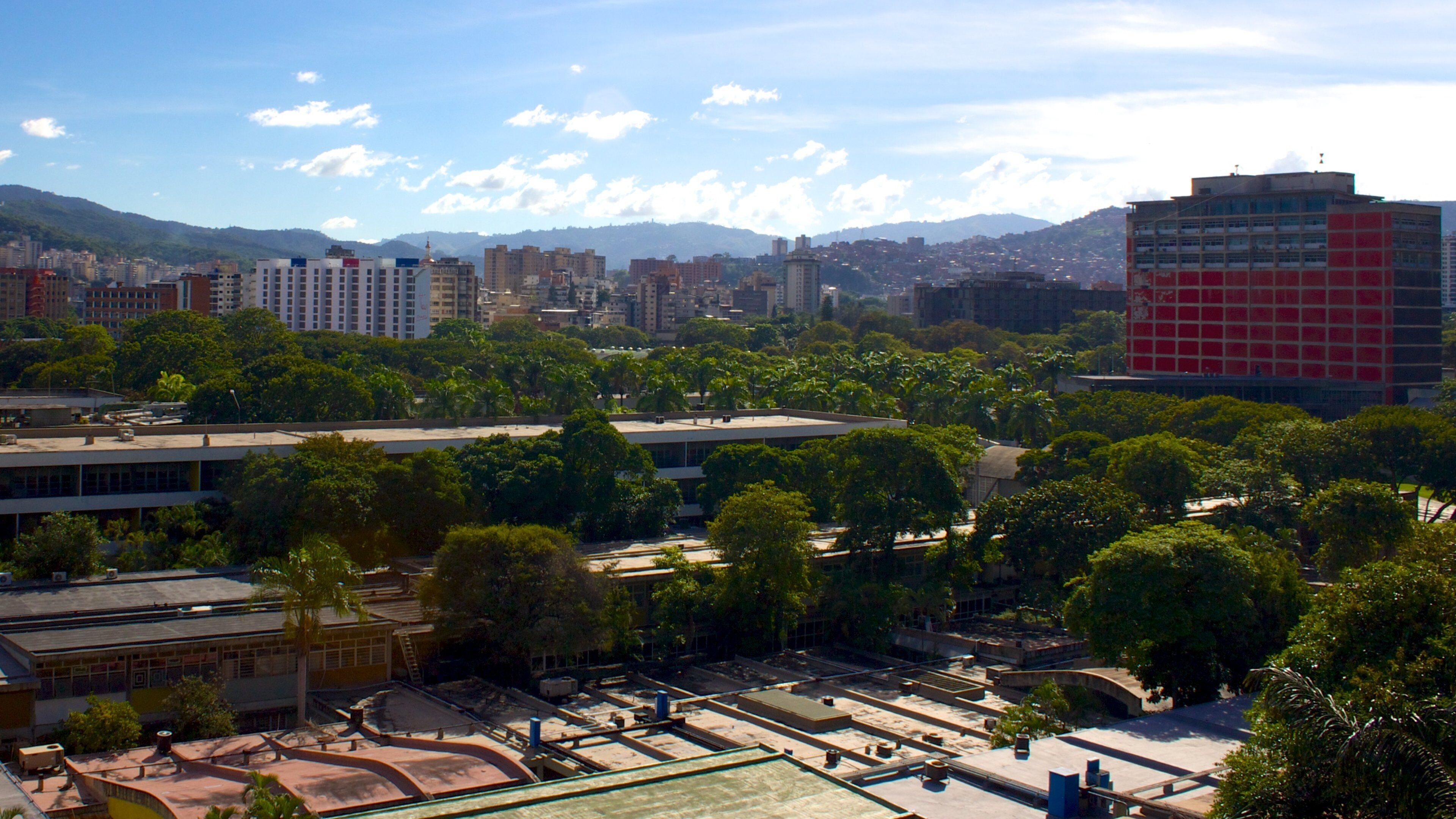 A cityscape with a mix of modern and older buildings, a large red building, and a mountainous backdrop.