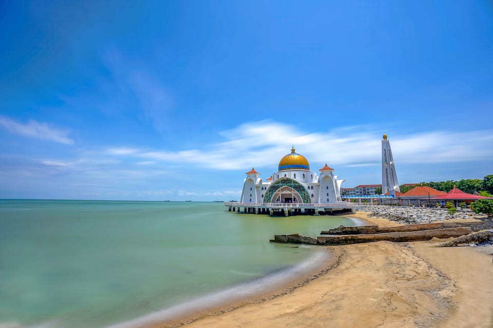 A white mosque with a golden dome and a tall minaret by the sea.