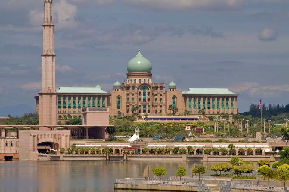 A large building with a tall minaret and multiple domes, surrounded by a body of water and greenery.