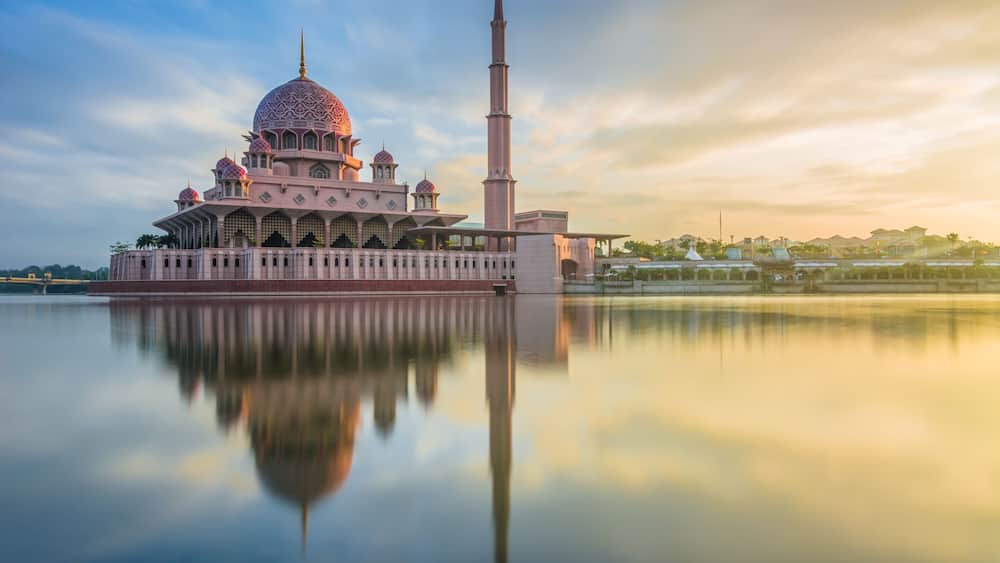 A mosque with a large dome and minarets, reflecting on calm water.