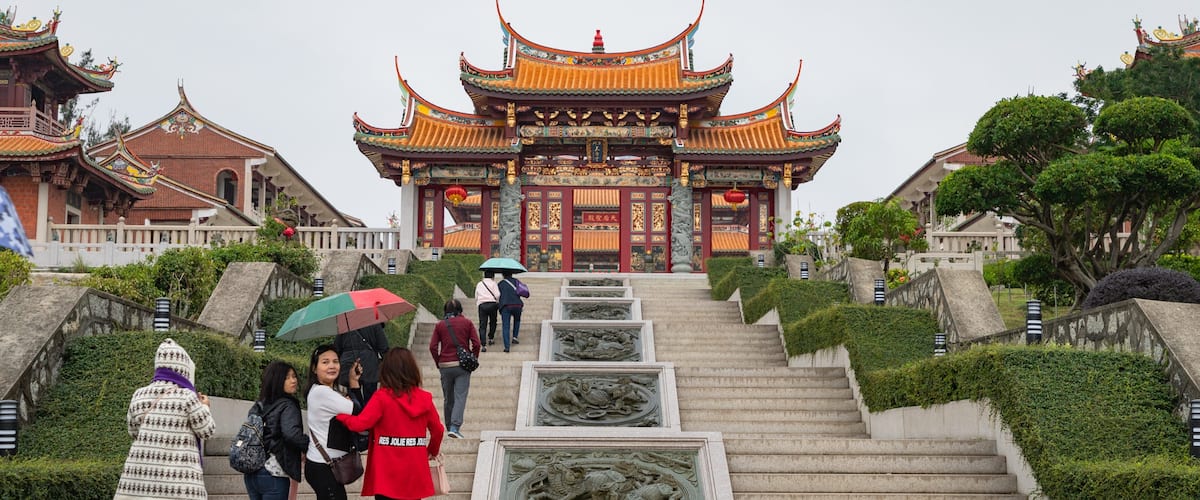 A traditional Chinese building with ornate architecture, a staircase leading up to it, and a statue in the foreground.