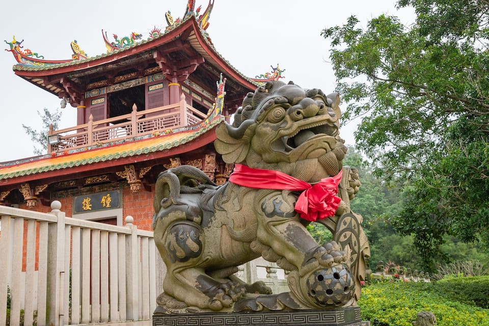 Un edificio tradicional chino con arquitectura elaborada y una estatua de león de piedra.