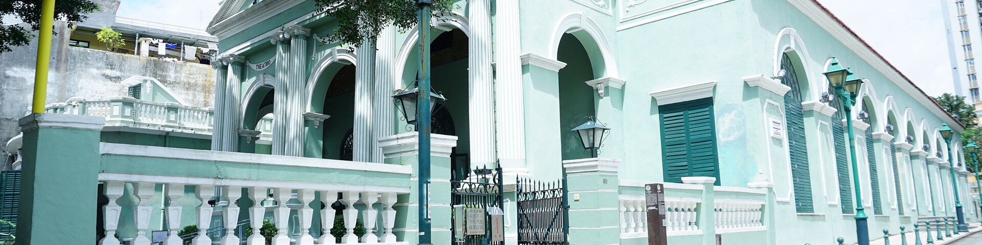 Um edifício histórico com fachada verde, janelas em arco e varanda com balaústres brancos.