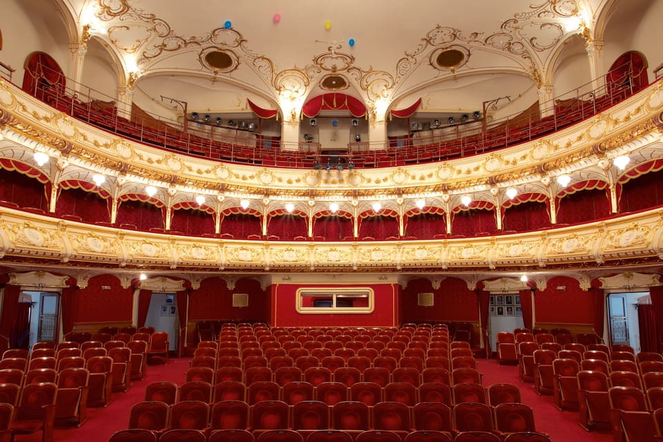 An ornate theater with red velvet seats and gold detailing.