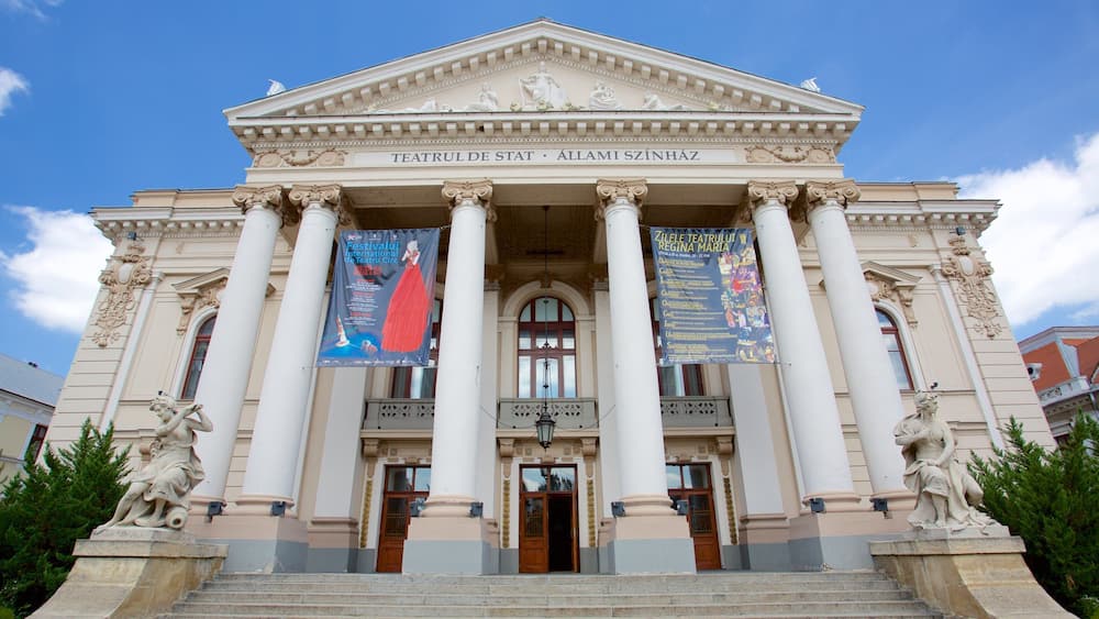 Ein neoklassizistisches Gebäude mit Säulen und Statuen, mit Bannern, die ein internationales Theaterfestival bewerben.