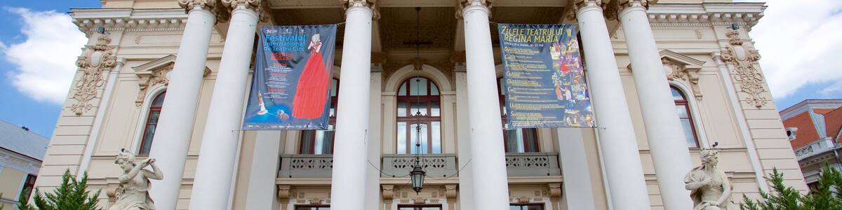 A neoclassical building with columns and statues, featuring banners advertising an international theater festival.