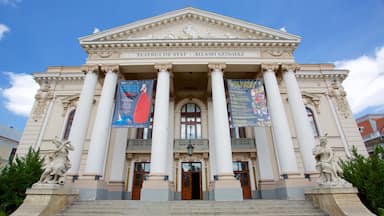 Un edificio neoclásico con columnas y estatuas, con pancartas que anuncian un festival internacional de teatro.