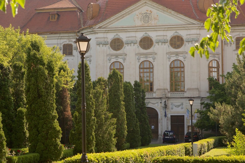 A historic building with ornate architecture, surrounded by well-maintained hedges and tall trees.