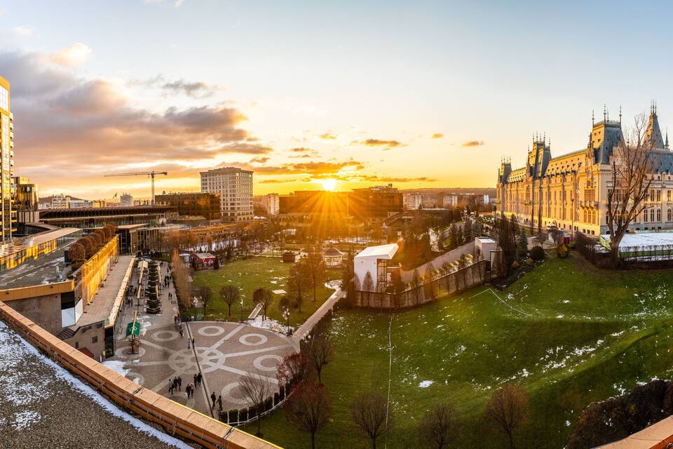 Paesaggio urbano con un edificio storico, un grattacielo moderno e un parco innevato.