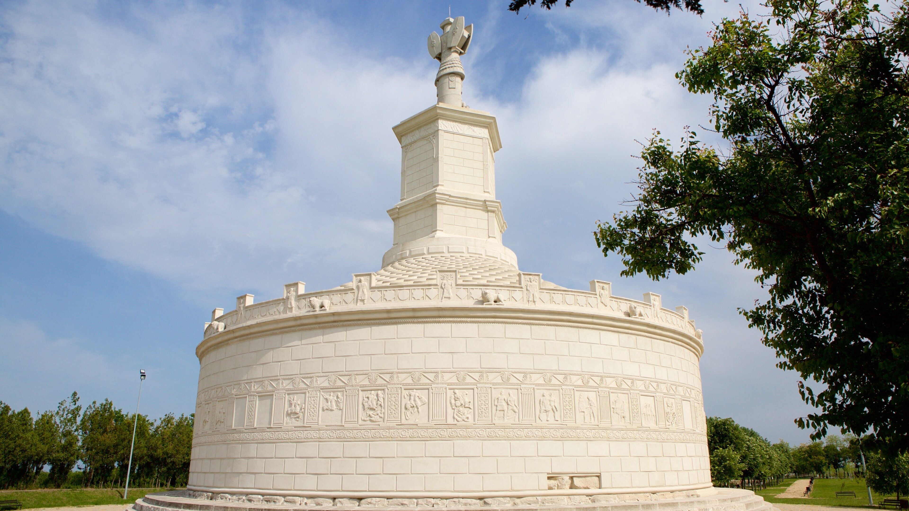 Um monumento branco e circular, com esculturas detalhadas e uma alta torre.