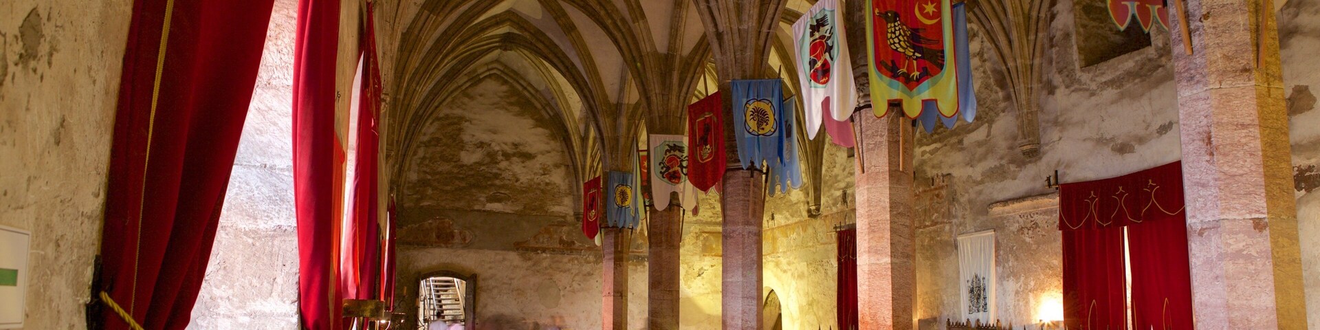 Interior de una catedral con altos techos abovedados, cortinas rojas y estandartes coloridos.
