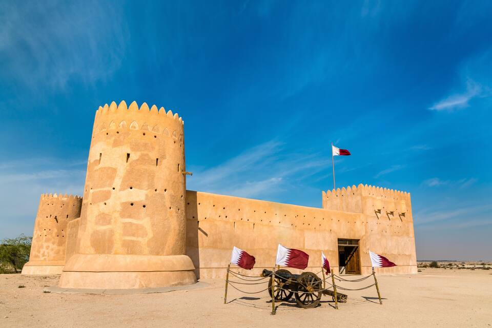 A historical fort with large towers and a flagpole, set against a clear blue sky.